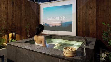 A person relaxing in a hot tub with a projection screen displaying the word 'essential' in the background.