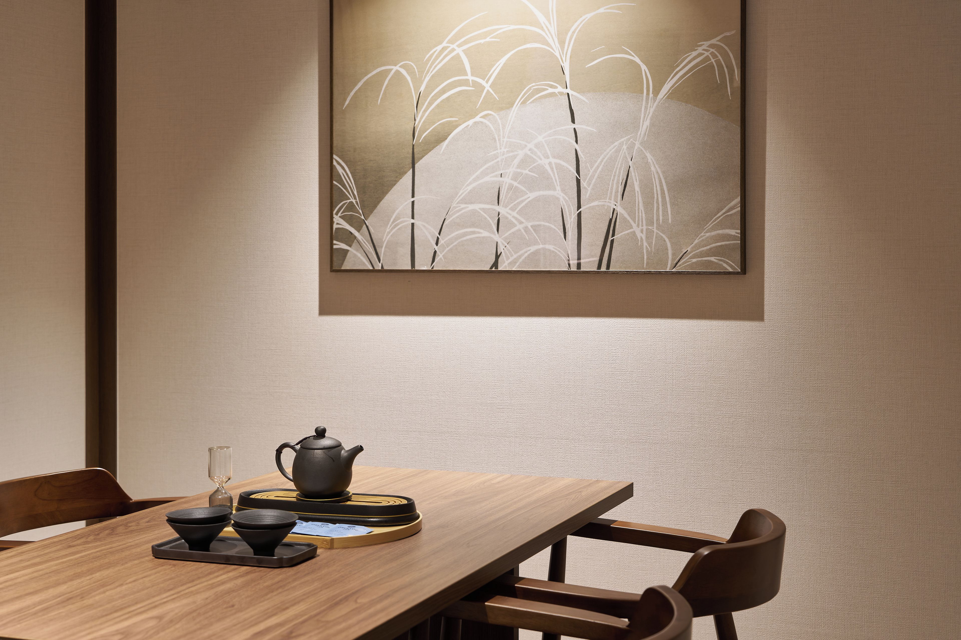 A dining area with a wooden table, chairs, a teapot, cups, and a framed artwork on the wall.