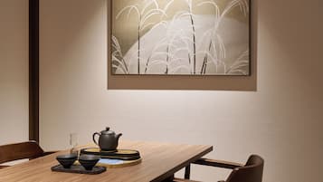 A dining area with a wooden table, chairs, a teapot, cups, and a framed artwork on the wall.
