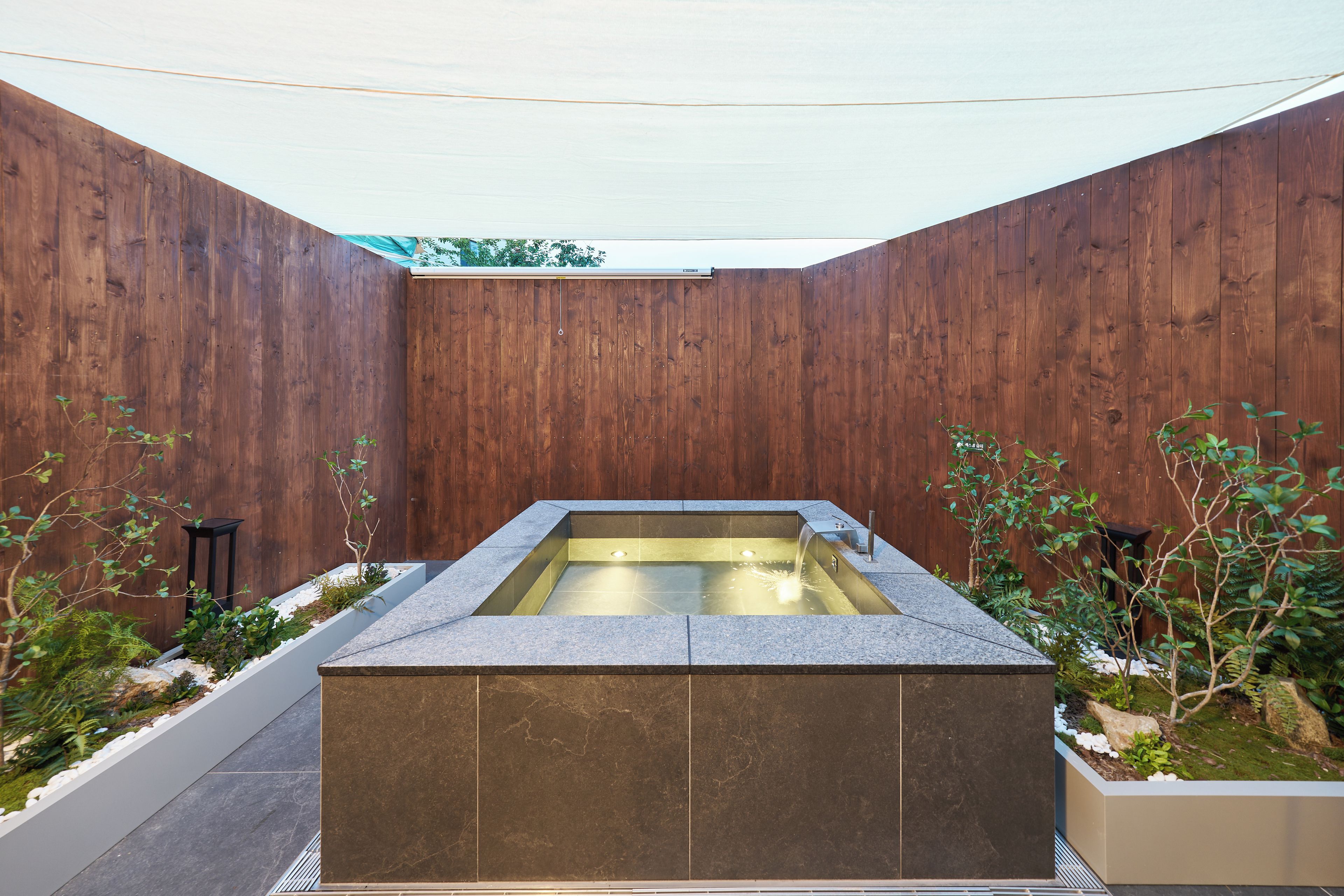 A rectangular hot tub with a stone exterior, surrounded by wooden walls and plants.