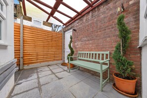 A patio area with a wooden fence, a bench, and potted plants. - Cozy East Ham Studio | 2 Double Beds | Sleeps 4 (Greater London)