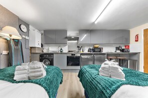 Eine moderne Küche mit Mikrowelle, Backofen und Waschmaschine. Es gibt zwei Betten mit grünen Decken.