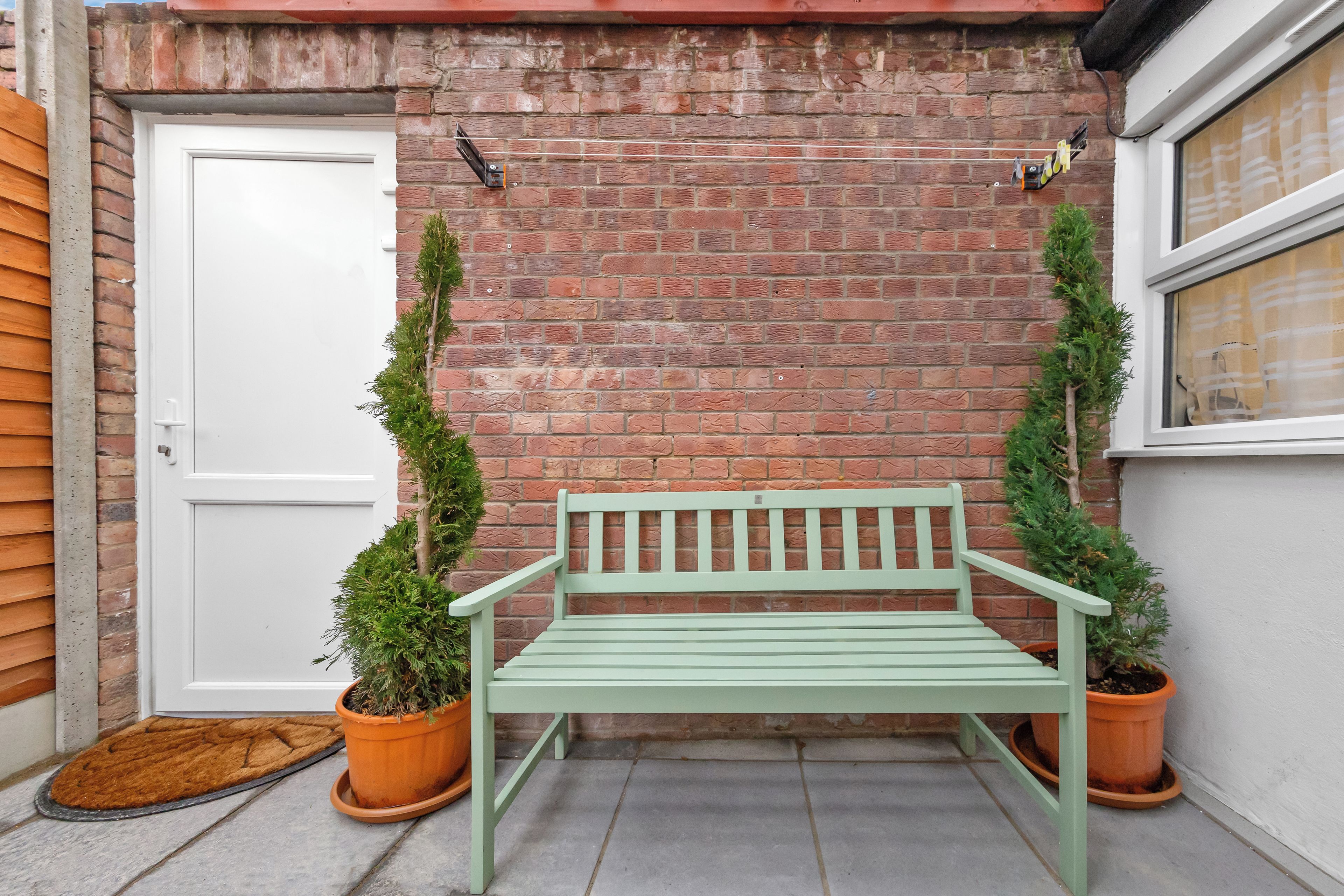 Un banc vert devant un mur de briques, avec une porte et une fenêtre blanches.