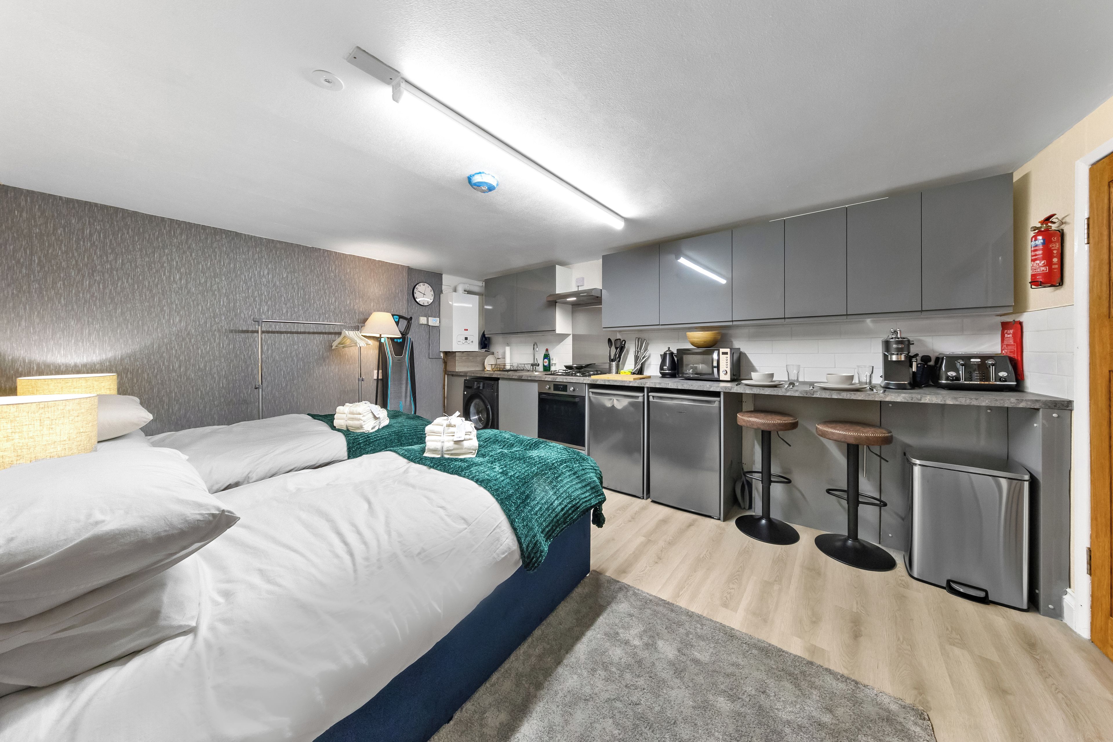 A modern hotel room with a bed, a desk, a kitchenette, and a bathroom.
