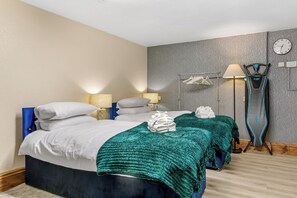 A hotel room with a bed, two bedside tables, a lamp, a clock, and a towel rack. - Cozy East Ham Studio | 2 Double Beds | Sleeps 4 (Greater London)
