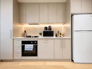 Cozinha moderna com armários brancos, forno embutido, micro-ondas e geladeira.