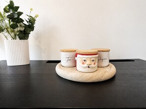 Eine Küchenarbeitsplatte mit drei Keramikbehältern mit Deckeln, einer weißen gerippten Vase mit Grünpflanzen und einem dunklen Holztisch.