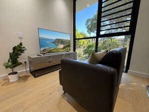 Ein modernes Wohnzimmer mit einem großen Flachbildfernseher, einem dunkelbraunen Ledersofa, Holzboden, einem weißen Konsolentisch und einer Topfpflanze.