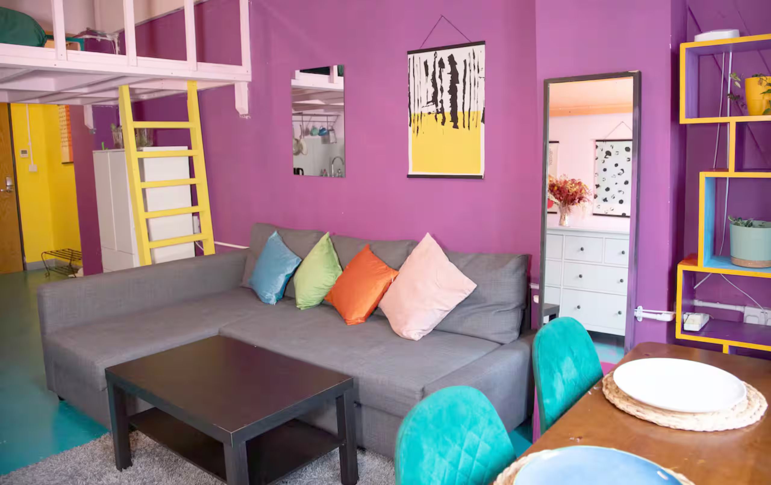 A room with a grey sofa, colorful cushions, a small table, and a yellow ladder.
