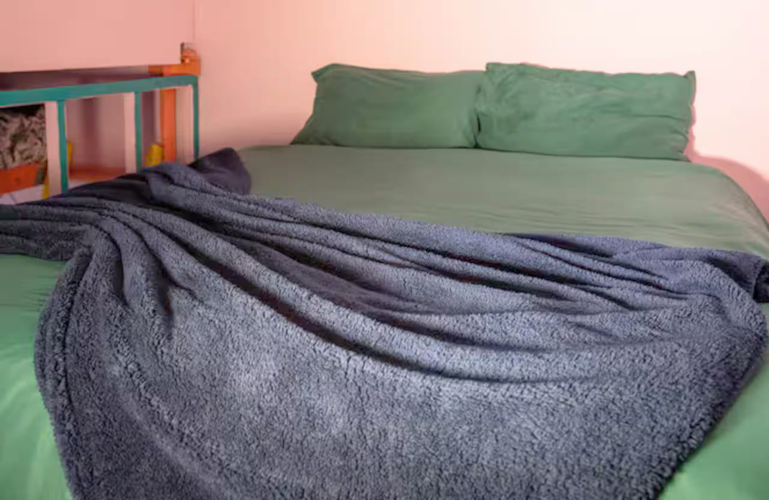 A bed with a green sheet and a dark blanket.