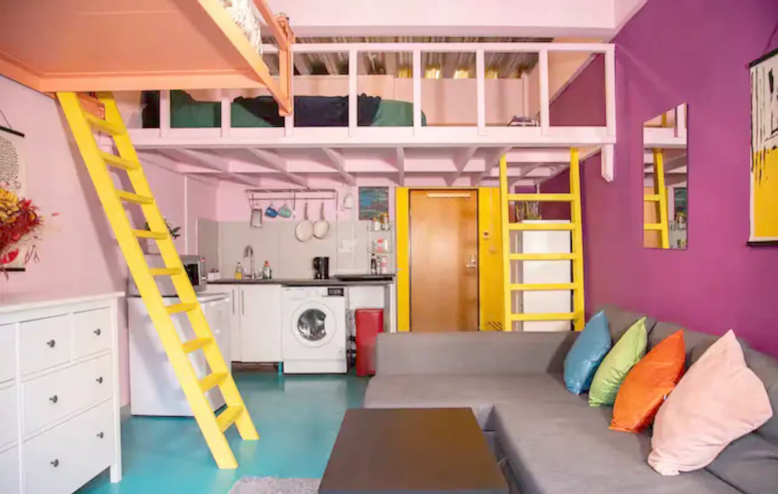 A multi-level room with a bunk bed, a kitchen area, and a sofa with colorful cushions.