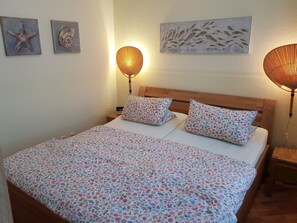 A bedroom with a wooden headboard, floral bedding, two bedside lamps, and wall art. - Holiday Apartment With 2 Bedrooms (Sellin)