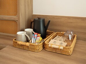 A wicker tray with a kettle, mugs, coffee packets, and sugar packets on a wooden floor. - Breezy North Pattaya (Pattaya)