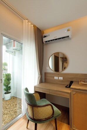 A room with a wooden desk, a chair, a round mirror, an air conditioning unit, and a potted plant. - Breezy North Pattaya (Pattaya)