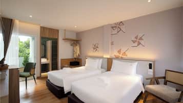 A hotel room with two beds, a sitting area with a chair, a small table, and a window with curtains.