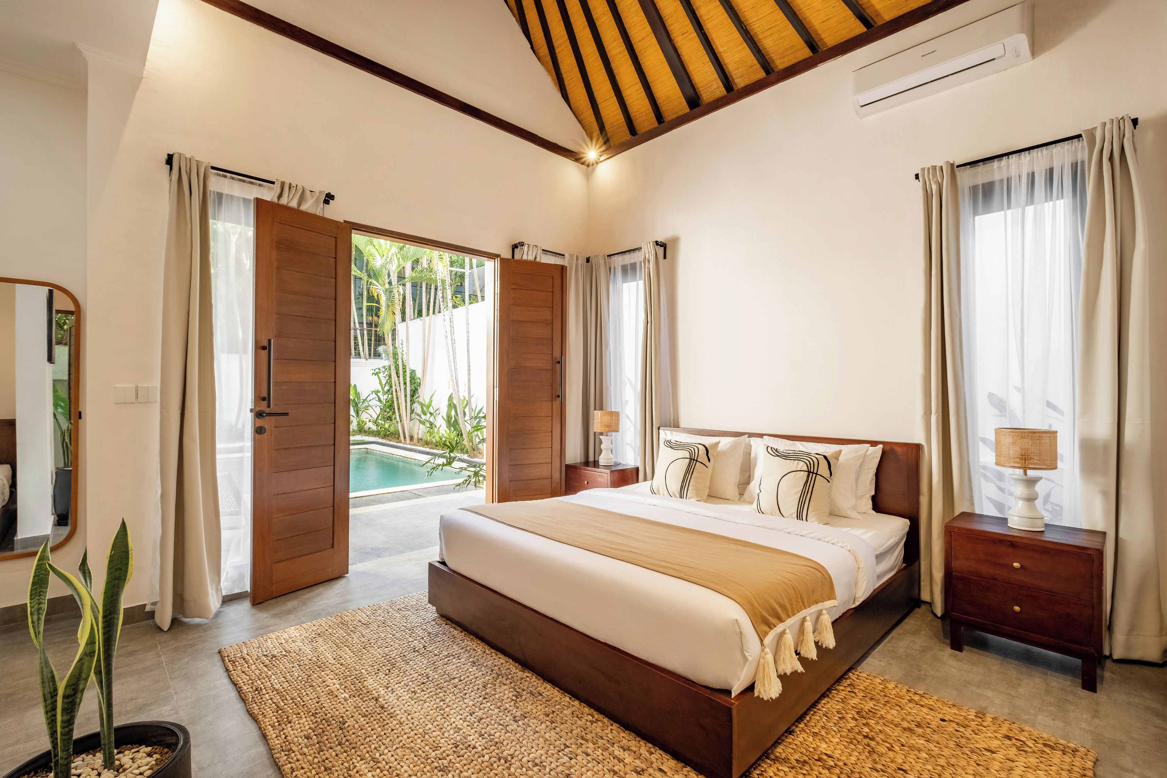 Quarto espaçoso com cama grande, cabeceira de madeira e vista para uma piscina.