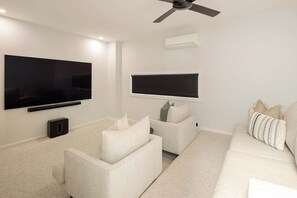 Ein modernes Wohnzimmer mit einem Flachbildfernseher, einem Deckenventilator und einem großen Fenster.