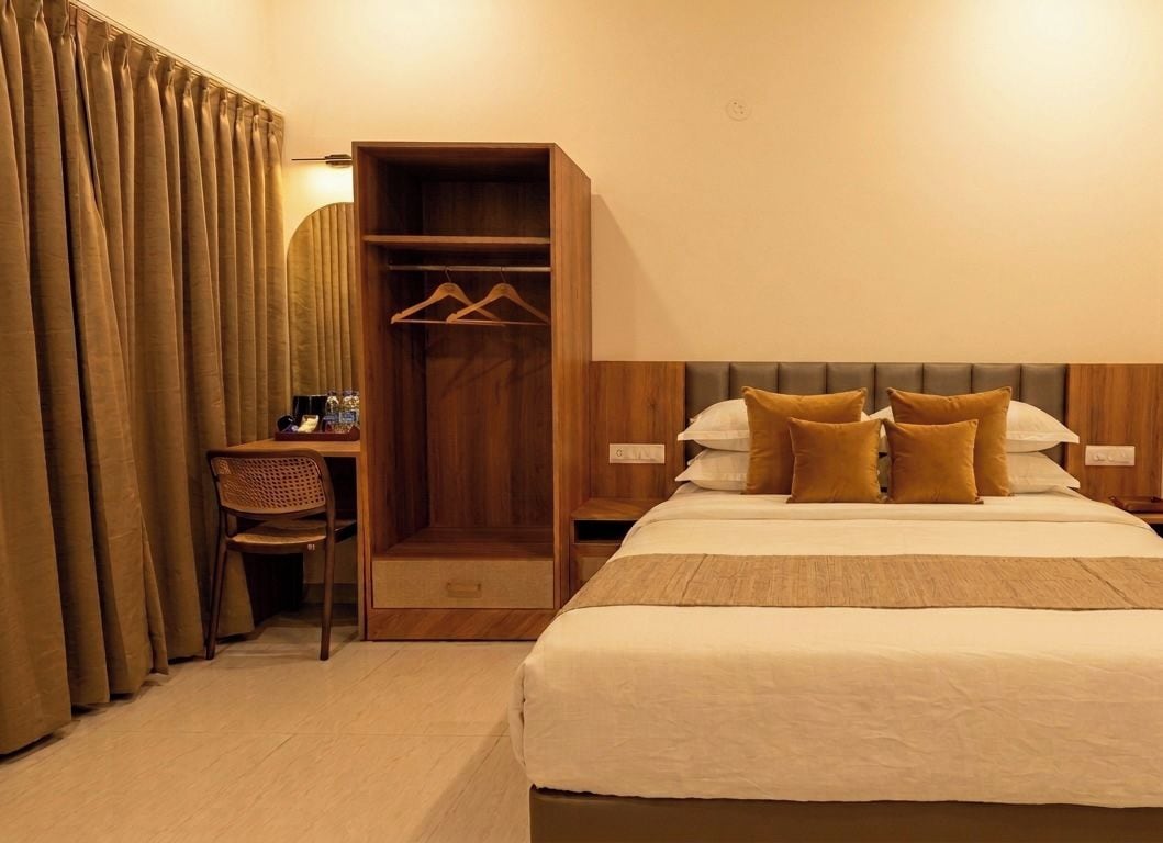 Quarto de hotel com cama, guarda-roupa de madeira, secretária e uma cadeira.