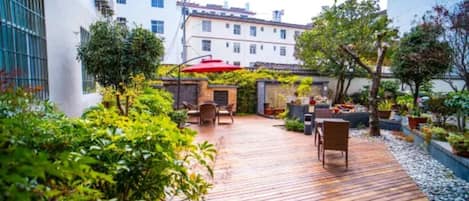 Eine Terrasss mit Holzboden, umgeben von viel Grün und einem roten Sonnenschirm.