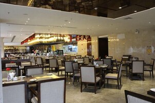 Restaurante com várias mesas e cadeiras, um bar e uma cozinha ao fundo.