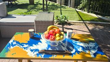 An outdoor patio with a colorful table, a wicker chair, and a small plant.