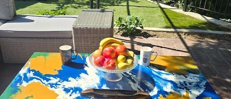 Un patio al aire libre con una mesa de colores, una silla de mimbre y una pequeña planta.