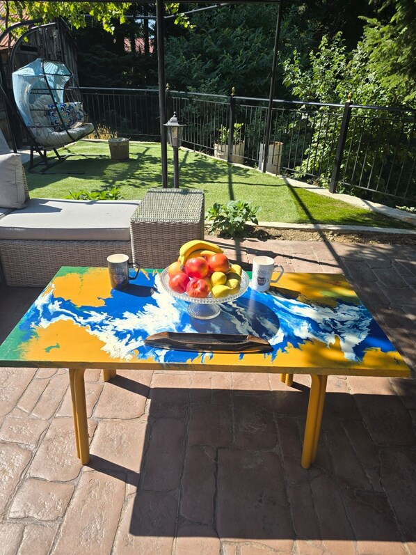 An outdoor patio with a colorful table, a wicker chair, and a small plant.