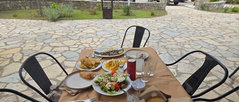 Una mesa para comer al aire libre con distintos platos, una botella y salero.