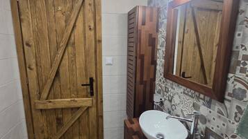 A bathroom with a wooden door, a sink with a mirror, and patterned tiles on the walls.