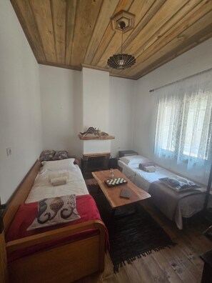 A small, cozy room with a wooden ceiling, a bed with a red blanket, a table with a chessboard, and a window with sheer curtains. - Oniropagida House in Beautiful Nature (Central Tzoumerka)
