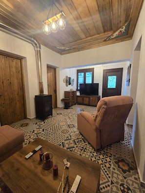 A living room with a patterned floor, a television, a sofa, and a wooden ceiling. - Oniropagida House in Beautiful Nature (Central Tzoumerka)