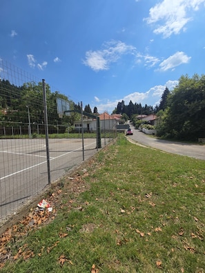 A fenced sports court with a road leading to houses, surrounded by trees and a clear sky. - Oniropagida House in Beautiful Nature (Central Tzoumerka)