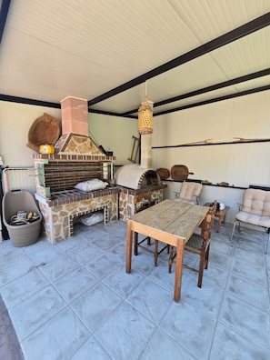An outdoor patio with a stone-built barbecue area, a wooden table, and cushioned chairs. - Oniropagida House in Beautiful Nature (Central Tzoumerka)