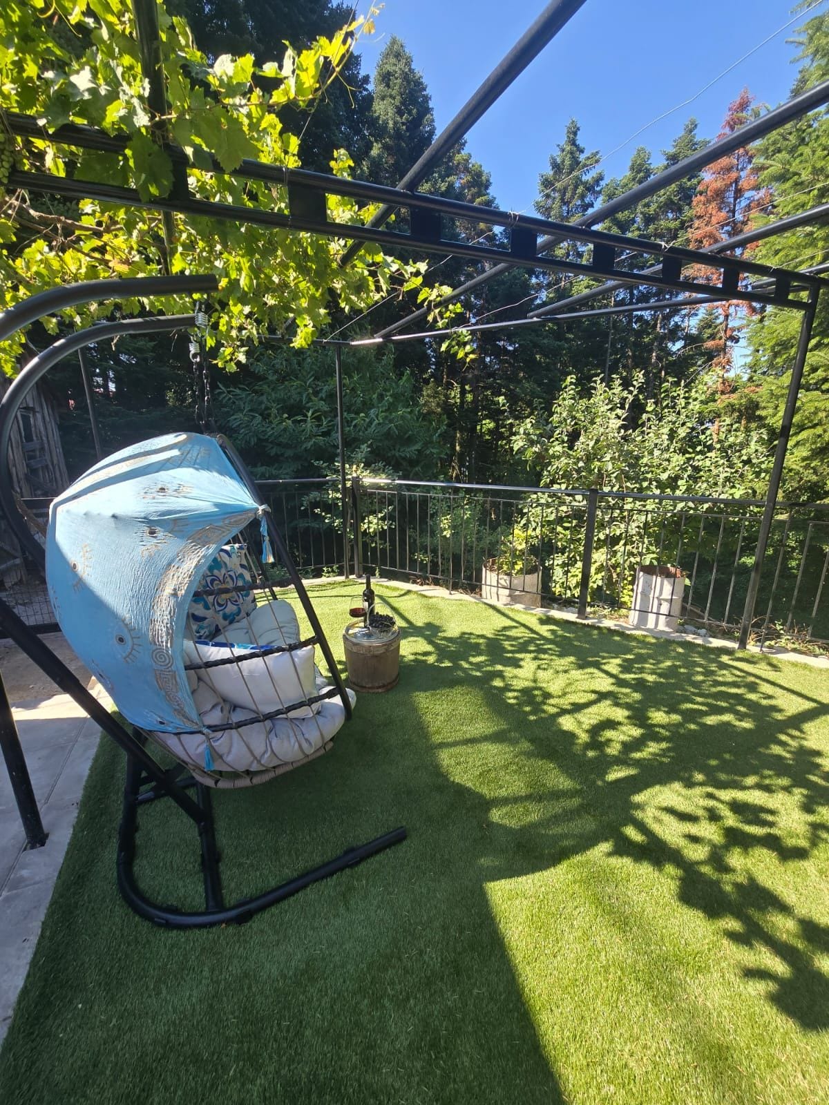 A garden with artificial grass, a swing set, and a pergola structure.