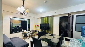 A modern living room with a dining area, a sofa, a TV, and a water dispenser. - Tranquil 2-Bedroom Apartment with Shared Pool in Davao City (Davao City)