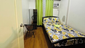 A small, single-bed room with a wooden floor, a chair, a desk, and a window with curtains. - Tranquil 2-Bedroom Apartment with Shared Pool in Davao City (Davao City)