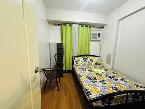 Una habitación pequeña con cama individual, piso de madera, una silla, un escritorio y una ventana con cortinas.