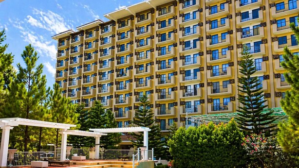 A hotel with a swimming pool, outdoor seating, and a large building with multiple balconies. - Spacious Davao City Apartment 3 Bedrooms, Pool, and Pine Trees (Davao City)