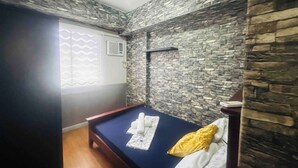 A room with a bed, a window with a view, and a stone wall. - Spacious Davao City Apartment 3 Bedrooms, Pool, and Pine Trees (Davao City)