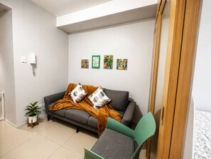 Ett modernt vardagsrum med en grå soffa, en grön fåtölj och en garderob i trä. På väggen hänger fyra konstverk och på golvet står en krukväxt.