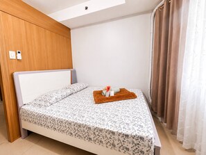 Uma cama de solteiro com colcha florida, uma toalha marrom e um pequeno objeto sobre a cama.