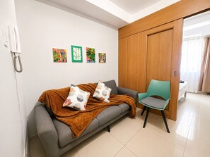 Uma área de espera moderna com um sofá cinzento, uma poltrona azul-esverdeada e um painel de madeira.