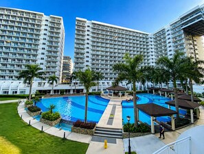A hotel with multiple high-rise buildings, a central swimming pool, and surrounding palm trees. - Urban Bliss 1BR Stay front of MOA at Shell Residence Tower C (Pasay City)