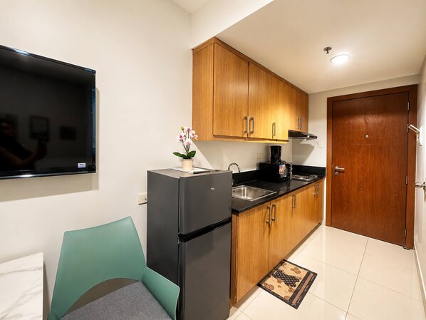 A compact kitchen with wooden cabinets, a black refrigerator, and a black countertop. - Urban Bliss 1BR Stay front of MOA at Shell Residence Tower C (Pasay City)