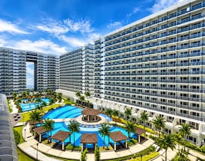 A multi-story hotel with a central pool area surrounded by palm trees and a circular pool. - Urban Bliss 1BR Stay front of MOA at Shell Residence Tower C (Pasay City)