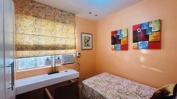 A small room with a desk, a bed, and two paintings on the wall.