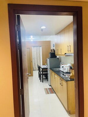 A kitchen with wooden cabinets, a dining table with chairs, and a refrigerator. - Fancy 1Br Condo Front of MOA IKEA at Shell  ResidencesTower B (Pasay)