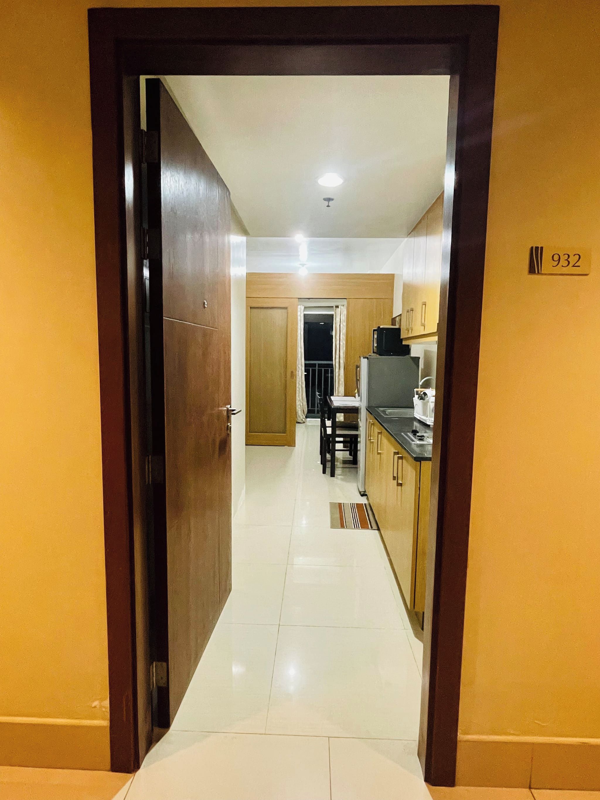 Pasillo de hotel que conduce a una cocina con mesa y sillas, un microondas y una cafetera.