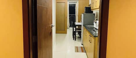 A hotel corridor leading to a kitchen area with a dining table and chairs, a microwave, and a coffee maker.