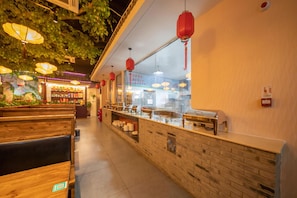 A restaurant interior with wooden benches, a counter with food items, and hanging red lanterns.